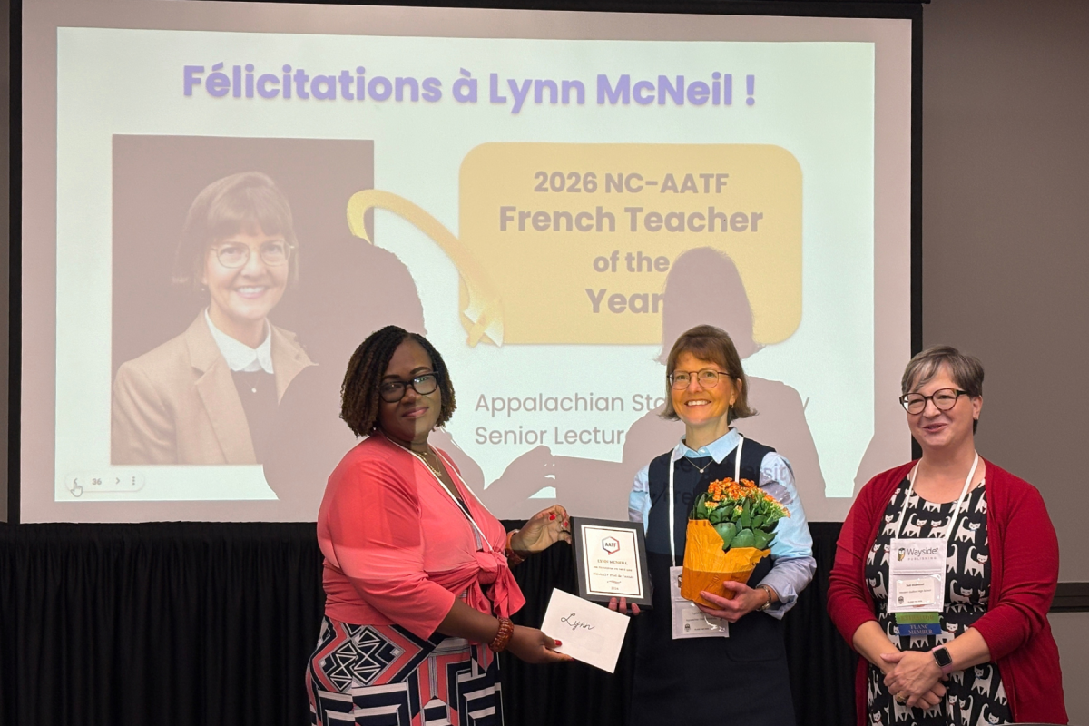 Three women pose beneath a &ldquo;F&eacute;licitations &agrave; Lynn McNeil!&rdquo; slide as Lynn receives the 2026 NC-AATF French Teacher of the Year award, flowers, and plaque.